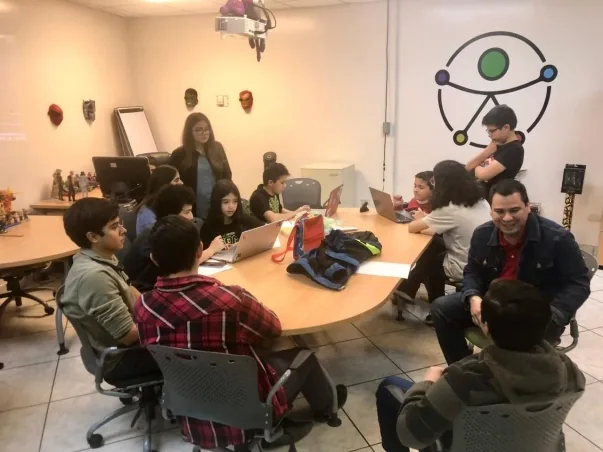 Mentoras y mentores trabajando con participantes del programa alrededor de una mesa.